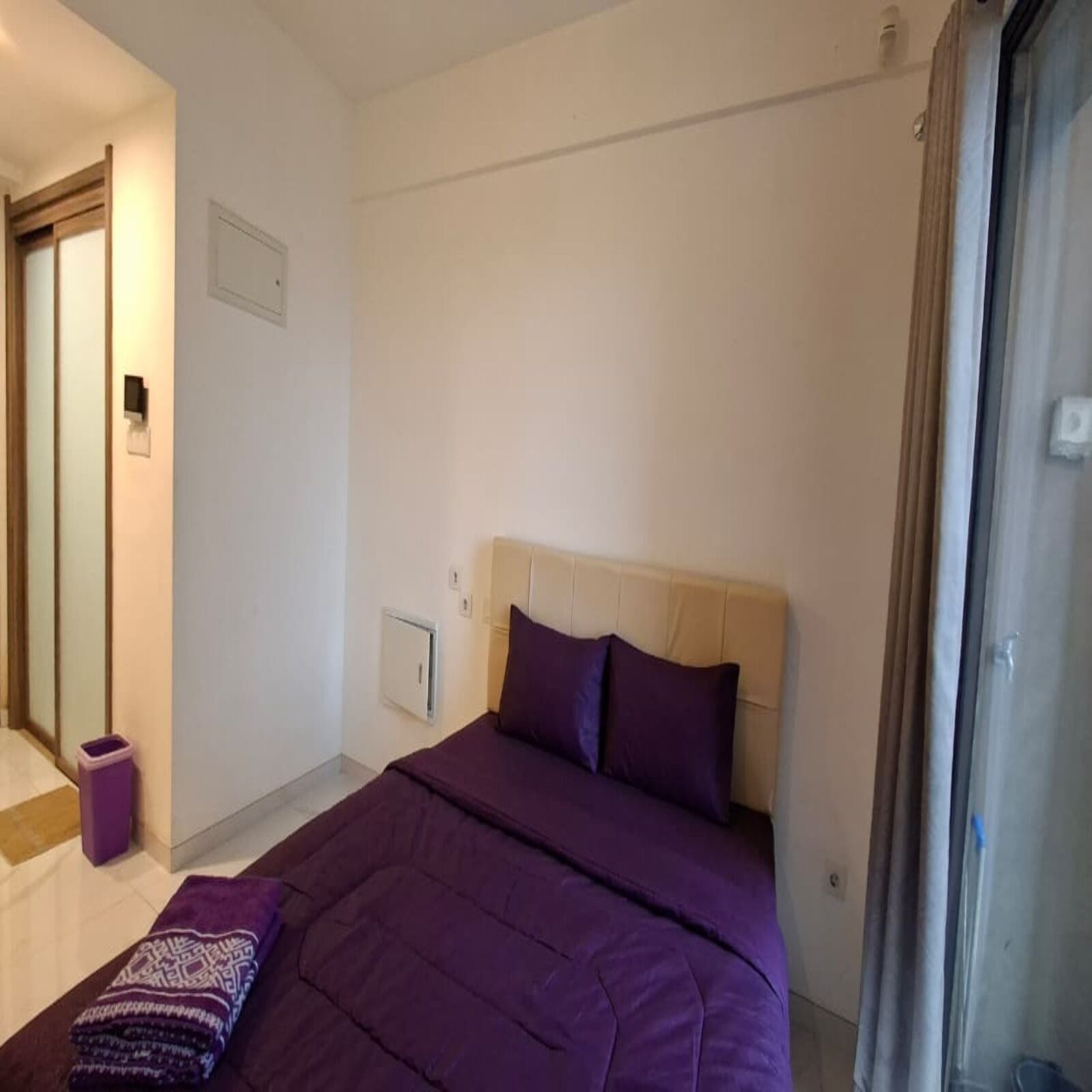 Ein Schlafzimmer mit einem Bett, einem Nachttisch, einem Papierkorb und einem Fenster.