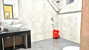 A bathroom with a white sink, a mirror, a red mop bucket, and a shower area. - Shiva solace by Sam Valley (Bhimtal)