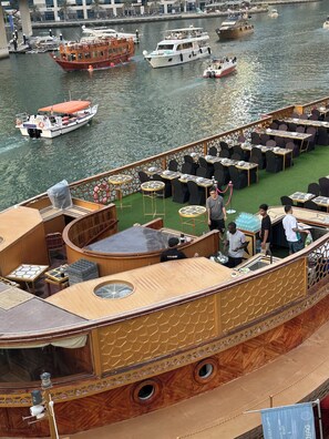 Een boot met een restaurantdek, compleet met tafels en stoelen, een bar en uitzicht op het water met andere boten.