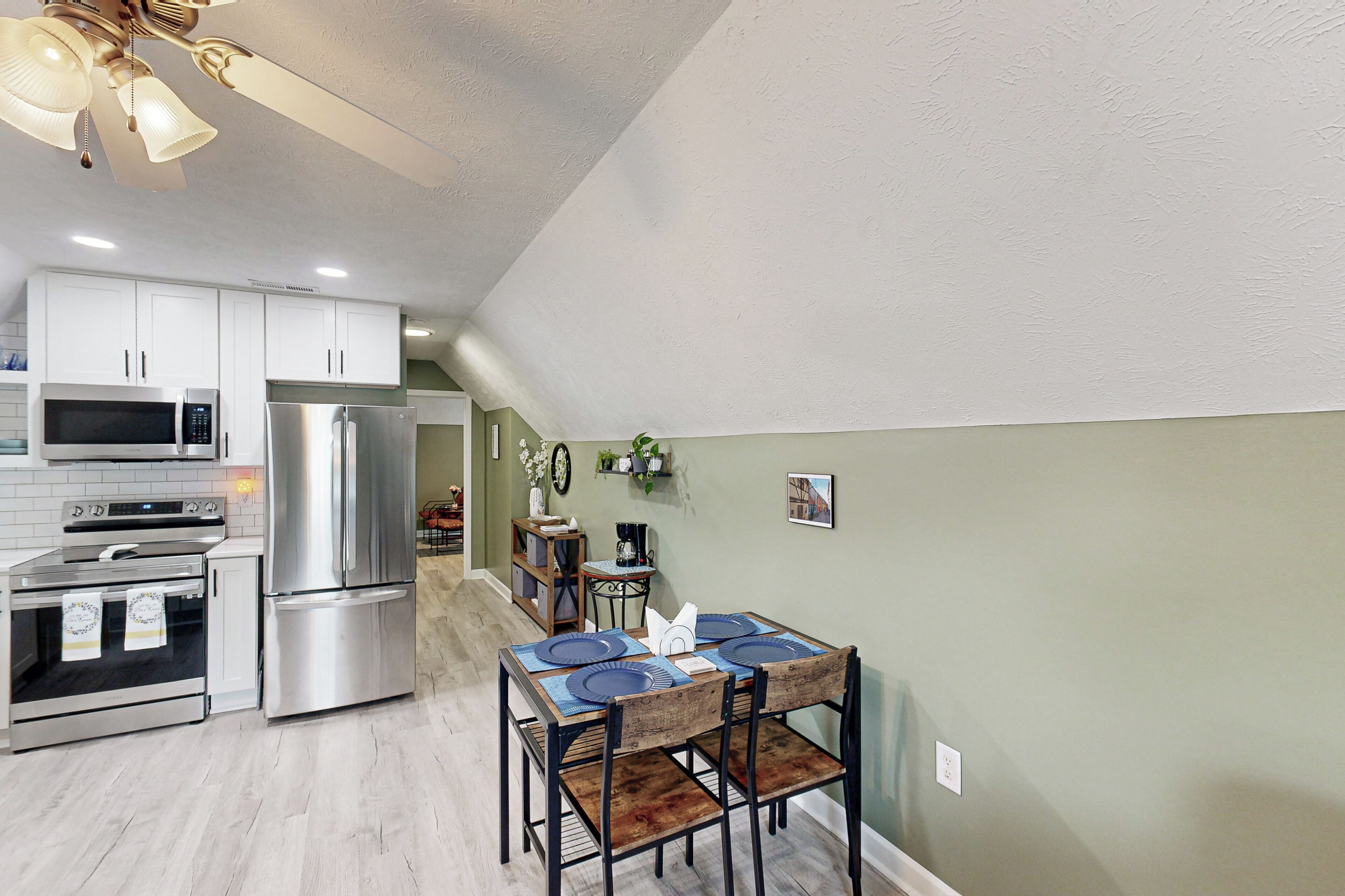 Een moderne keuken met roestvrijstalen apparatuur, een eethoek met houten stoelen en een groene accentmuur.