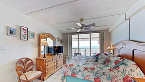 A bedroom with a bed, a dresser, a chair, a ceiling fan, and a window with a view. - Shorefront Resort Retreat: Suntide III - Unit 1002 (South Padre Island)