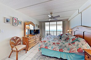 Quarto com cama, penteadeira, cadeira, ventilador de teto e janela com vista.