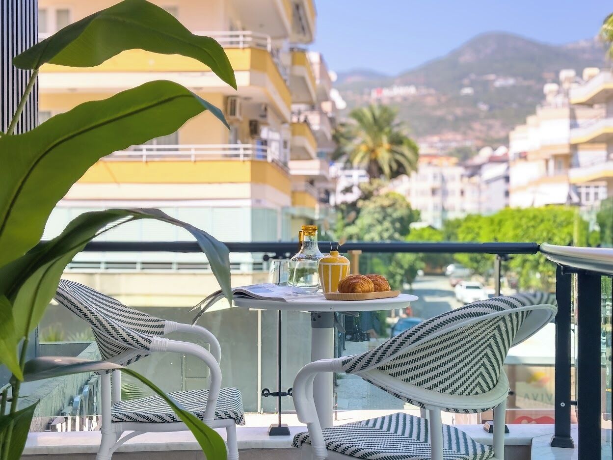 Un balcon avec des fauteuils en osier, une petite table avec une bouteille, un verre et des croissants.