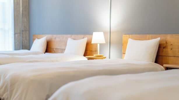 Une chambre d’hôtel avec deux lits, une tête de lit en bois, une table de chevet avec une lampe et un grand miroir au mur.