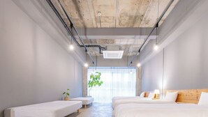 Habitación de hotel moderna con una cama grande, dos camas más pequeñas, un banco y un ventanal con vistas.