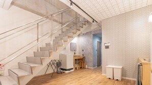 Un intérieur moderne avec un escalier en bois, un coin cuisine et une salle de bain dotée d’un lavabo et d’un porte-serviettes blancs.