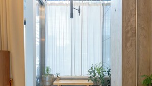 Un intérieur moderne avec un banc en bois, des plantes en pot et une grande fenêtre ornée de rideaux légers.