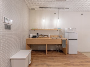 Eine kleine Küche mit Holztresen, Spüle, Mikrowelle und Kühlschrank. Hängelampen und eine Wand mit Ziegeloptik sind vorhanden.