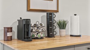 Een koffiehoek met een koffiezetapparaat, een muggenhouder, een koffiebus en een plant op een houten aanrecht.