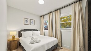 Een net opgemaakt bed met witte lakens, een bedlampje en een ingelijst beeld aan de muur.