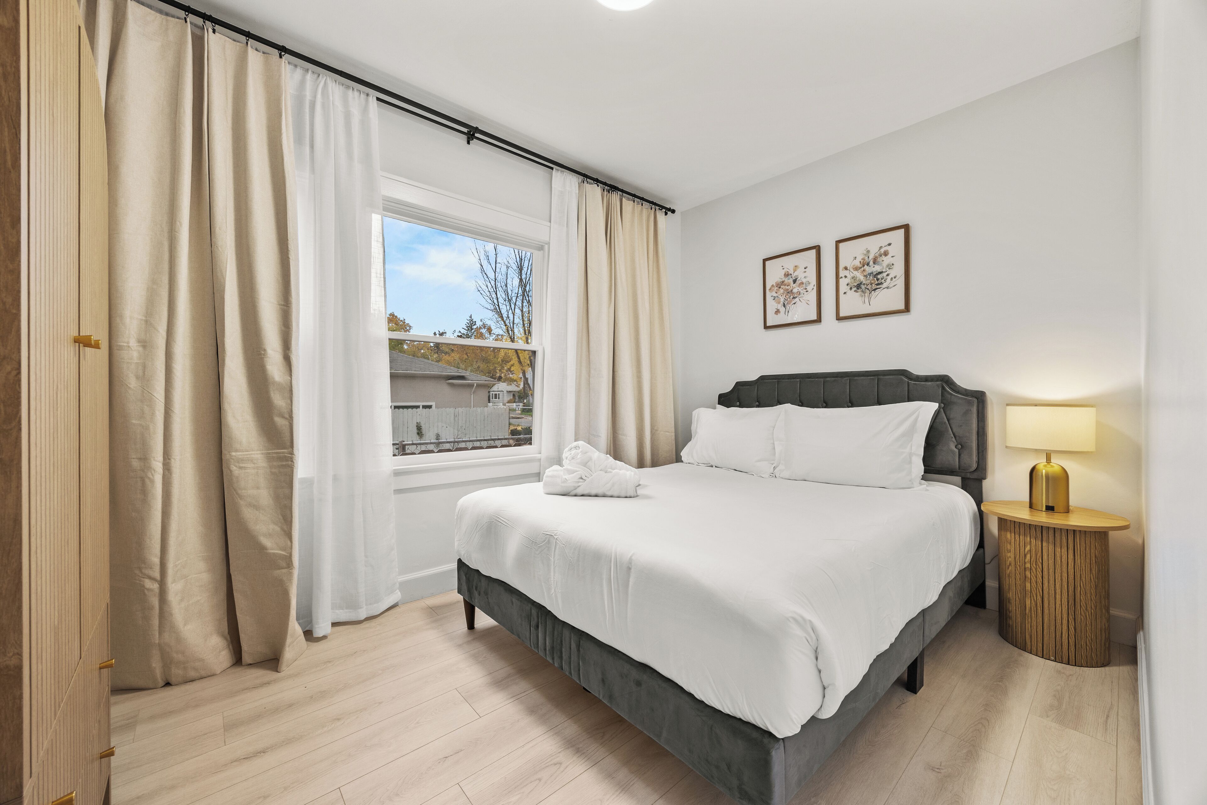 Un dormitorio con una cama grande, una mesita de noche con lámpara y una ventana con cortinas.