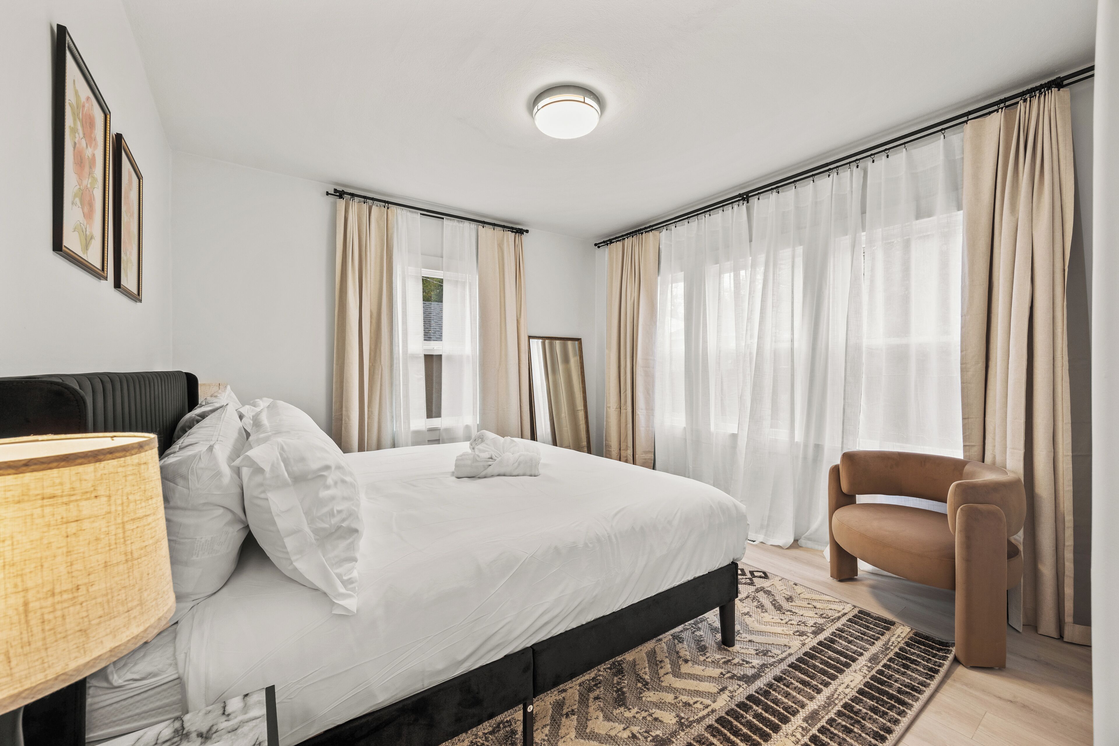 A modern bedroom with a large bed, a bedside table, a chair, and a patterned rug.
