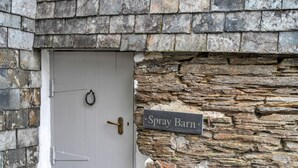 Una puerta blanca con manija de latón y un cartel que dice "Spray Barn" sobre una pared de piedra.
