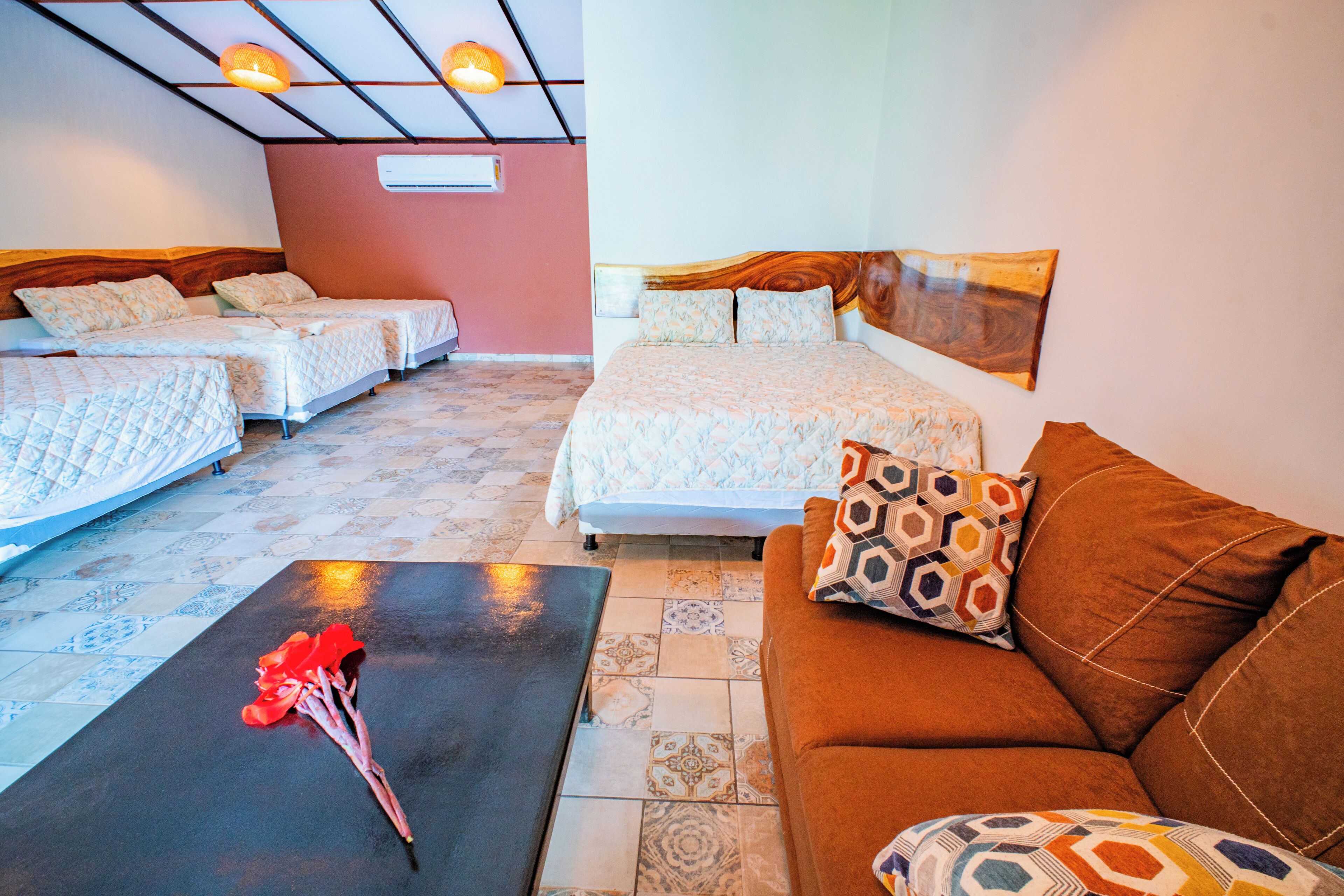 A hotel room with two single beds, a double bed, a brown sofa, and a black table with a vase of red flowers.