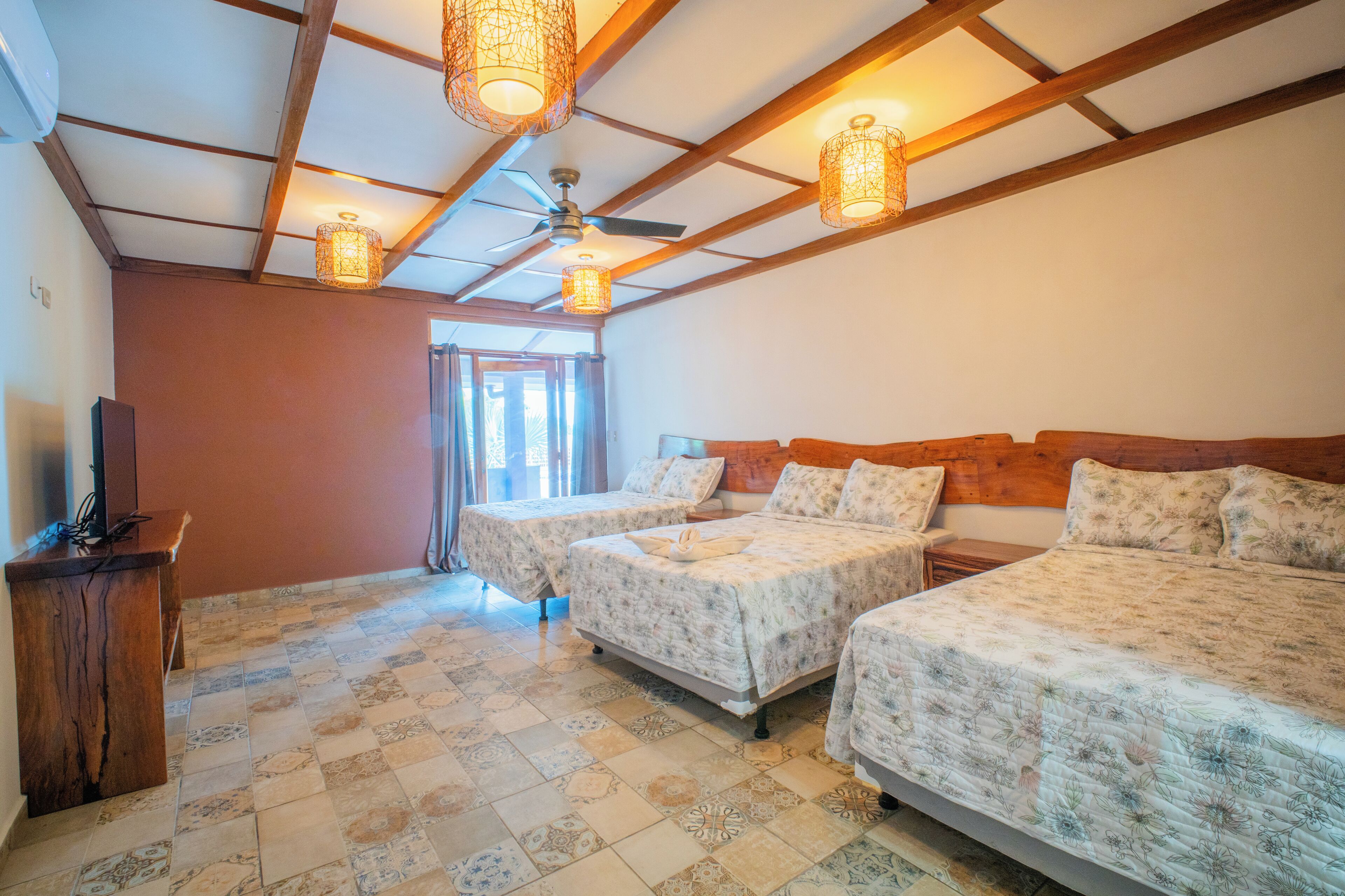 A hotel room with two beds, a wooden headboard, a ceiling fan, and a television on a wooden stand.