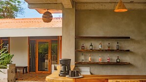 A kitchen area with a coffee maker, mugs, and a shelf with bottles. - Casa Las Flores (El Cuco)