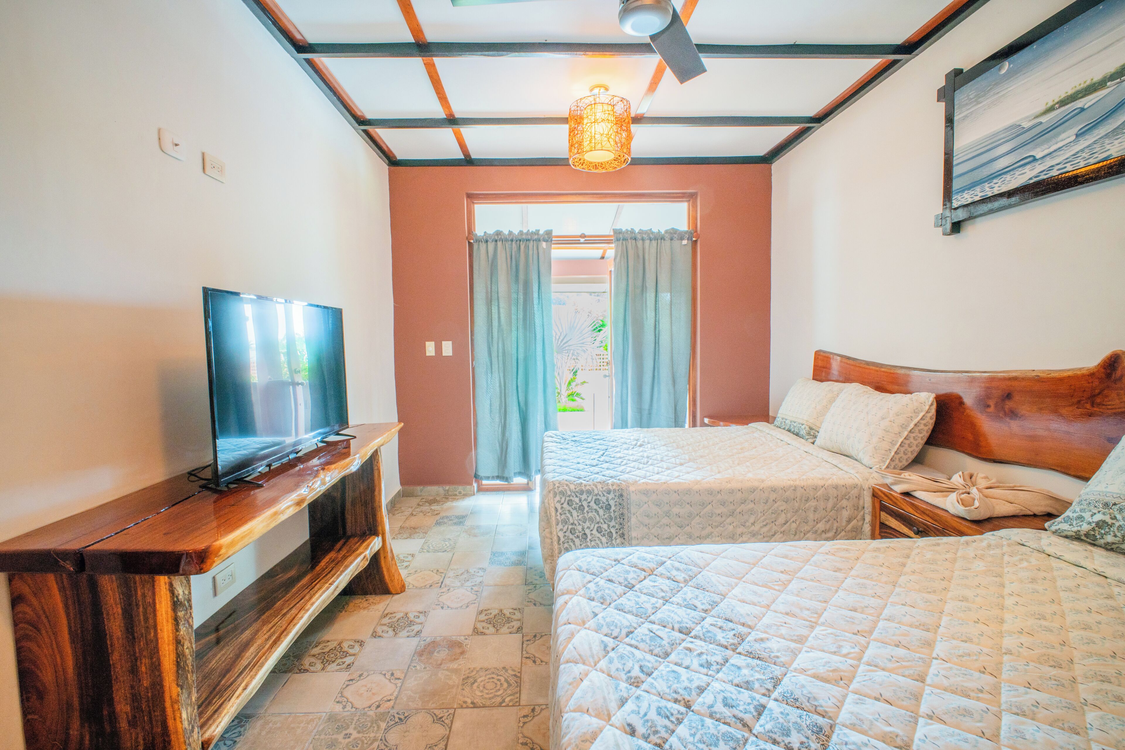 A bedroom with two beds, a TV on a wooden stand, and a ceiling fan.