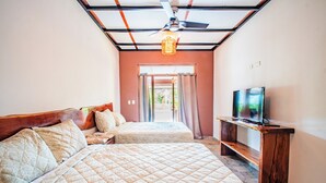 A bedroom with two beds, a ceiling fan, a TV on a wooden stand, and a view of the outdoors through a door. - Casa Las Flores (El Cuco)