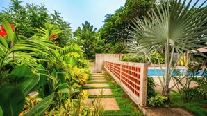 A garden pathway leading to a pool area with lush greenery and a concrete wall. - Casa Las Flores (El Cuco)