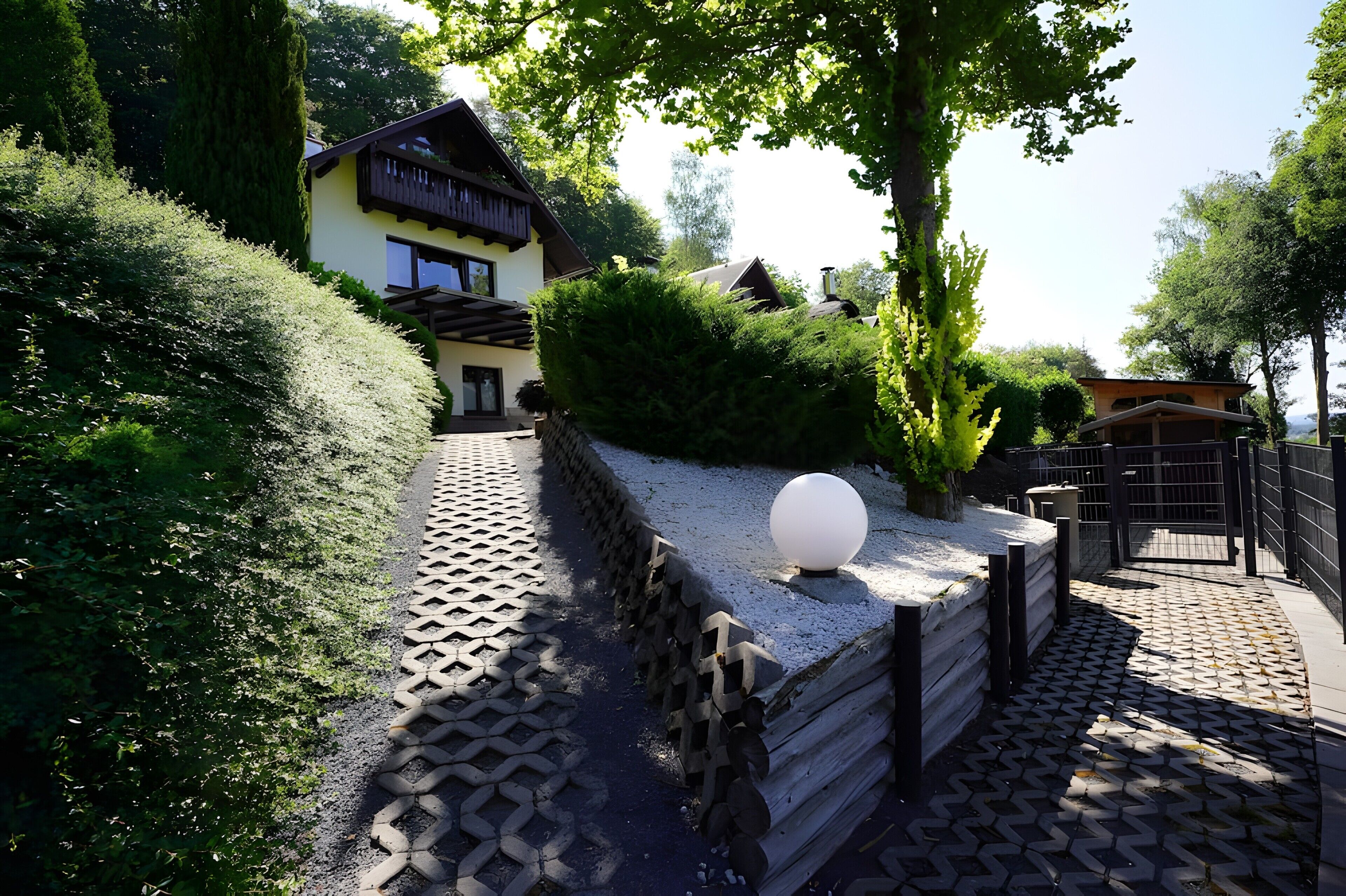 A traditional house with a wooden deck, surrounded by lush greenery and a paved pathway.