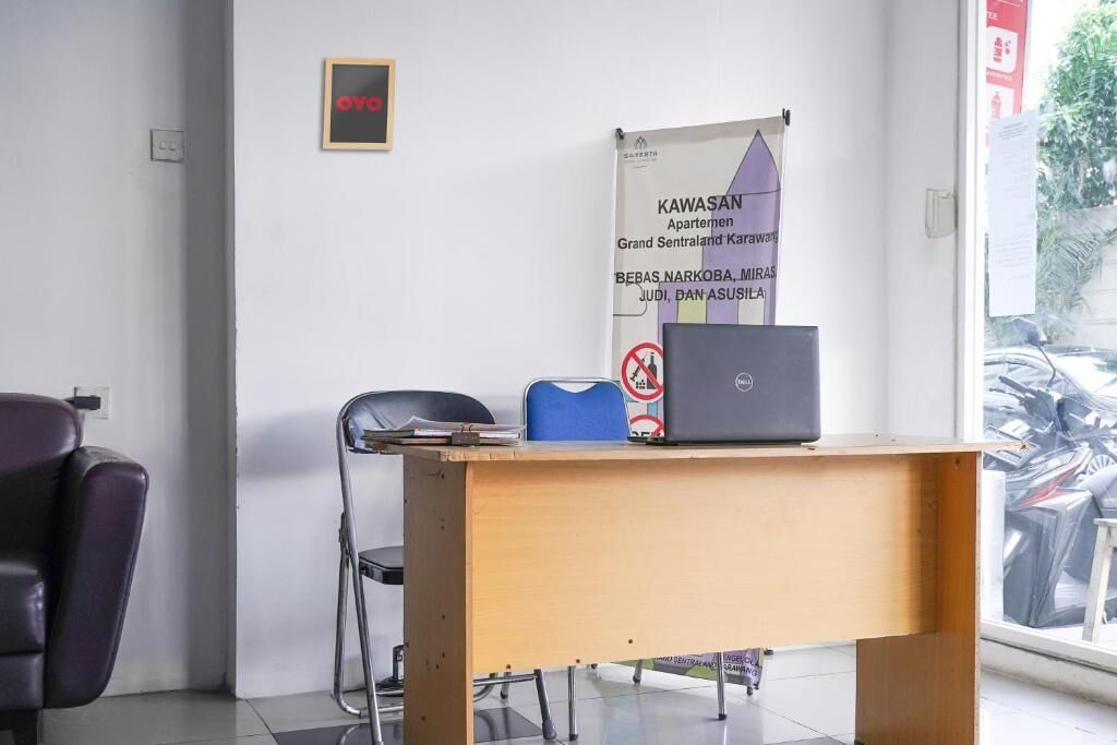Ein Zimmer mit einem Holztisch, einem Laptop, einem blauen Stuhl und einem schwarzen Stuhl. An der Wand hängt ein Banner mit Text.