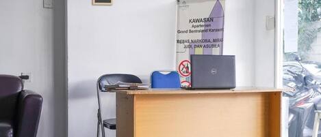 A room with a wooden desk, a laptop, a blue chair, and a black chair. A banner with text is on the wall.
