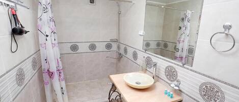 A bathroom with a shower, a sink with a mirror, and decorative tiles.