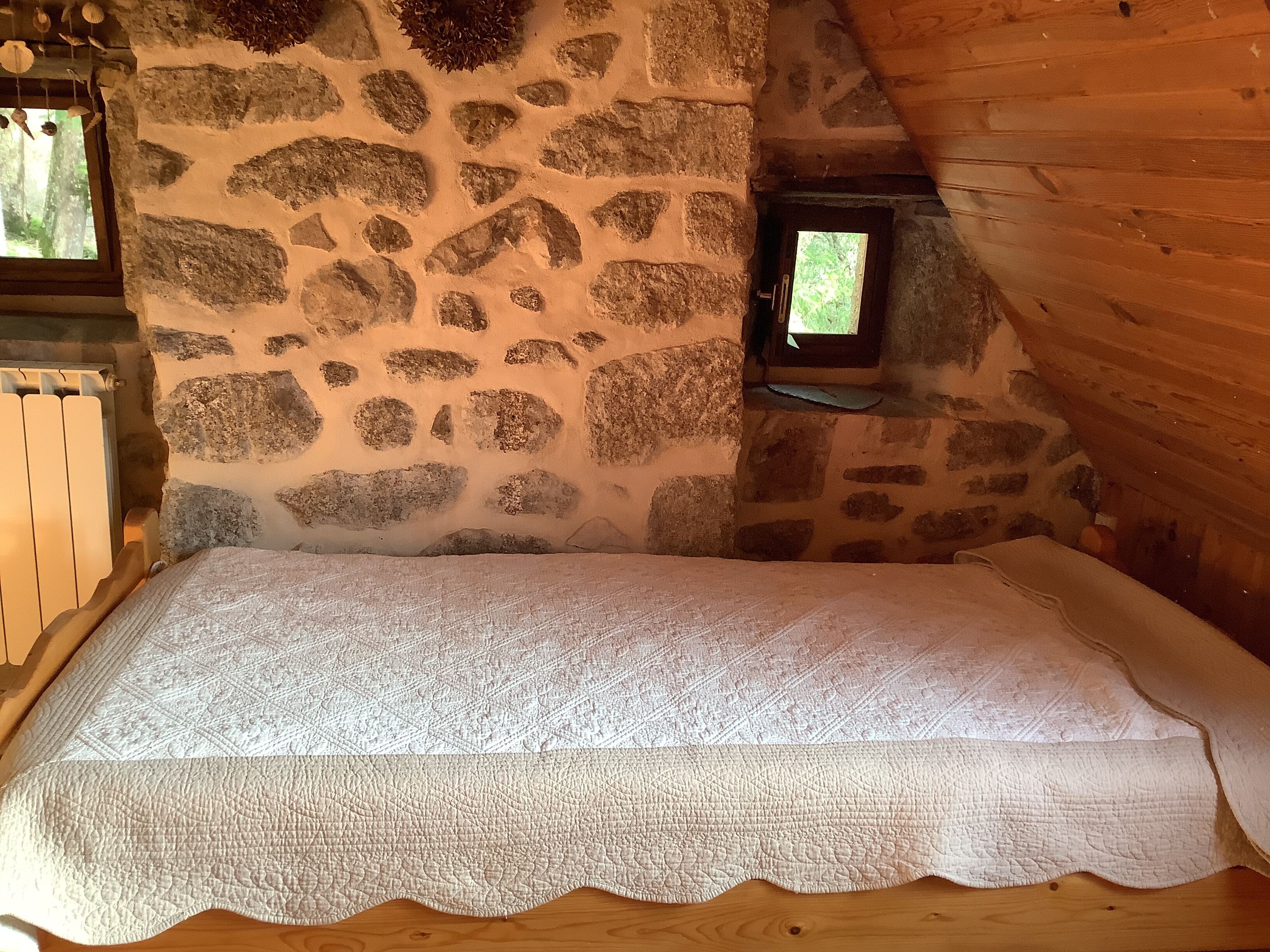 A cozy room with a stone wall, a small window, and a bed with a white quilt.