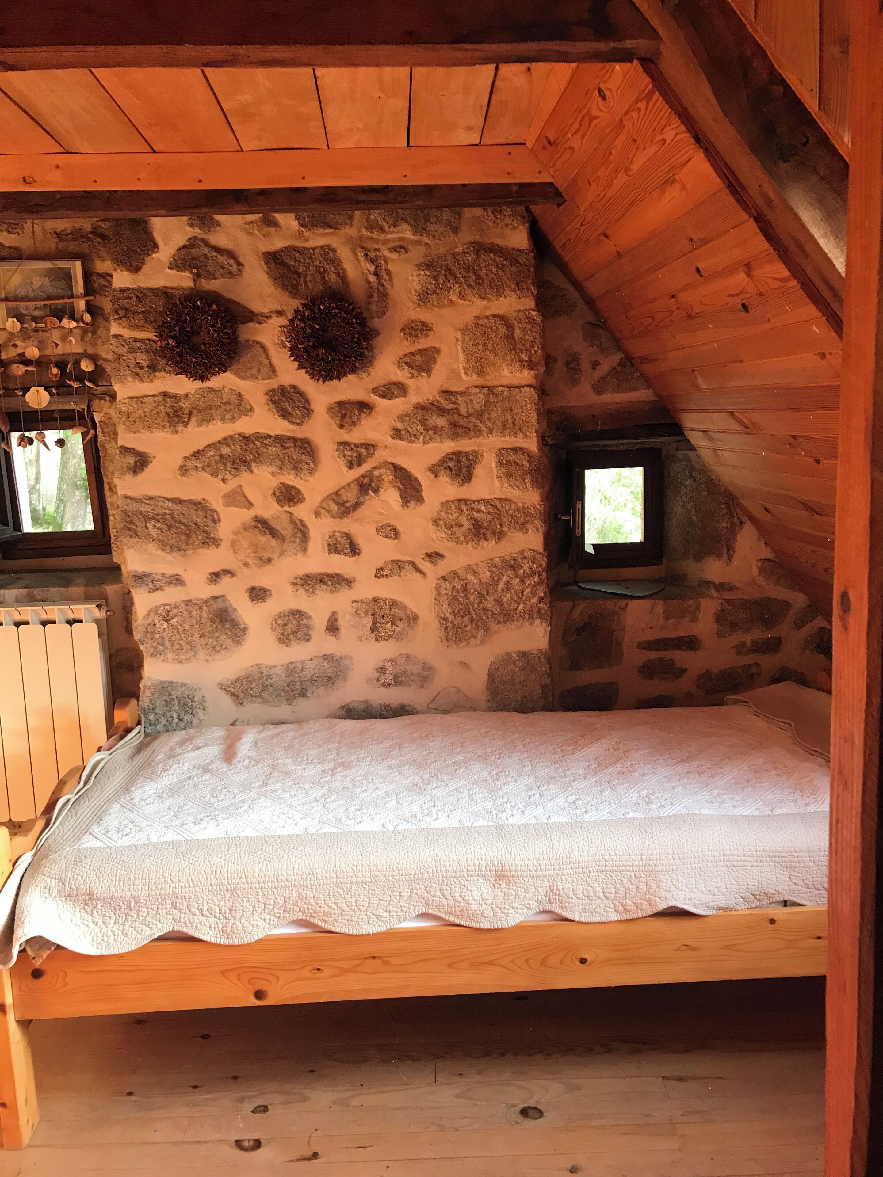 Un dormitorio acogedor en el ático, con pared de piedra, cama de madera y una ventana pequeña.
