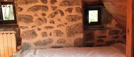 Un dormitorio acogedor en el ático, con pared de piedra, cama de madera y una ventana pequeña.
