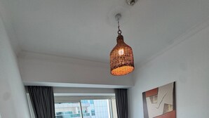 Ein modernes Schlafzimmer mit einem großen Bett, einer Stehlampe, Blick auf die Stadt durch ein großes Fenster und einer Deckenleuchte.