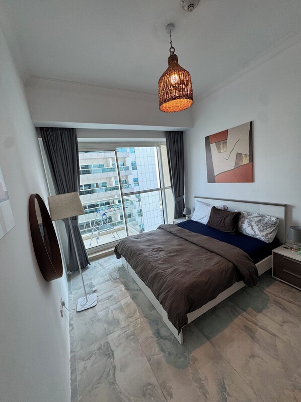 A modern bedroom with a large bed, a floor lamp, a view of the city through a large window, and a ceiling light fixture.