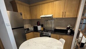 Eine moderne Küche mit Holzausbau, einem Edelstahlkühlschrank, einem Gasherd und einem Esstisch aus Marmor mit weißen Stühlen.