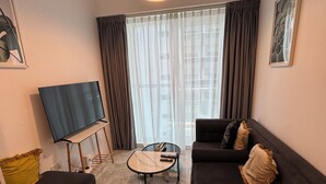 Ein Wohnzimmer mit einer Couch, einem Hocker, einem Couchtisch und einem Flachbildfernseher auf einem Standfuß.