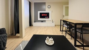 A modern living room with a flat-screen TV displaying Netflix, a dining area with a wooden table and chairs, and a black coffee table with a tray. - One-Bedroom Apartment in Taksim - No: 11 (Beyoglu)