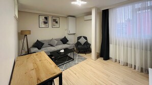 A modern living room with a sofa, coffee table, and a chair. There is a lamp, a cabinet, and a window with curtains. - One-Bedroom Apartment in Taksim - No: 11 (Beyoglu)