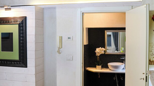 A modern interior with a wooden ceiling, a white brick wall, a gray sofa with green and white pillows, and a bathroom visible through an open door. - Casa Pannella (Vittorio Veneto)