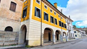A street with historic yellow and beige buildings, featuring arched doorways and a clear sky. - Casa Pannella (Vittorio Veneto)