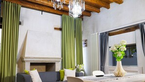 A modern living room with a fireplace, green curtains, a white vase with flowers, and a dining area. - Casa Pannella (Vittorio Veneto)