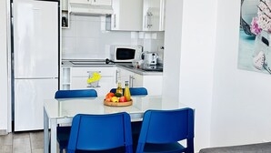 Una cucina moderna con mobili bianchi, un frigorifero, un forno a microonde e un'area pranzo con sedie blu e un tavolo in vetro.