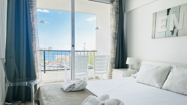Una camera d'albergo con un letto, due sedie, un tavolo e vista sul mare.