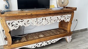 Un tavolo consolle in legno con decorazioni elaborate, un televisore a schermo piatto, una lampada decorativa e un orologio a parete.
