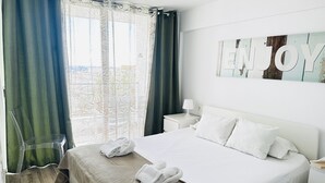 Una camera d'albergo con un letto, una sedia, un comodino, una lampada e vista sulla città.