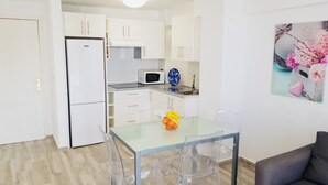 Una cucina compatta con mobili bianchi, un frigorifero bianco, un forno a microonde e un piccolo tavolo con sedie.