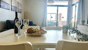 Uma área de refeições com uma mesa posta para dois, uma garrafa de vinho e uma tigela de frutas.