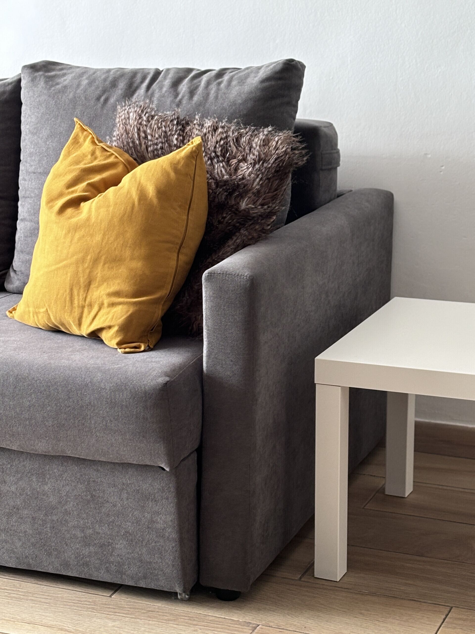 A grey sofa with a mustard yellow pillow and a fluffy grey pillow.