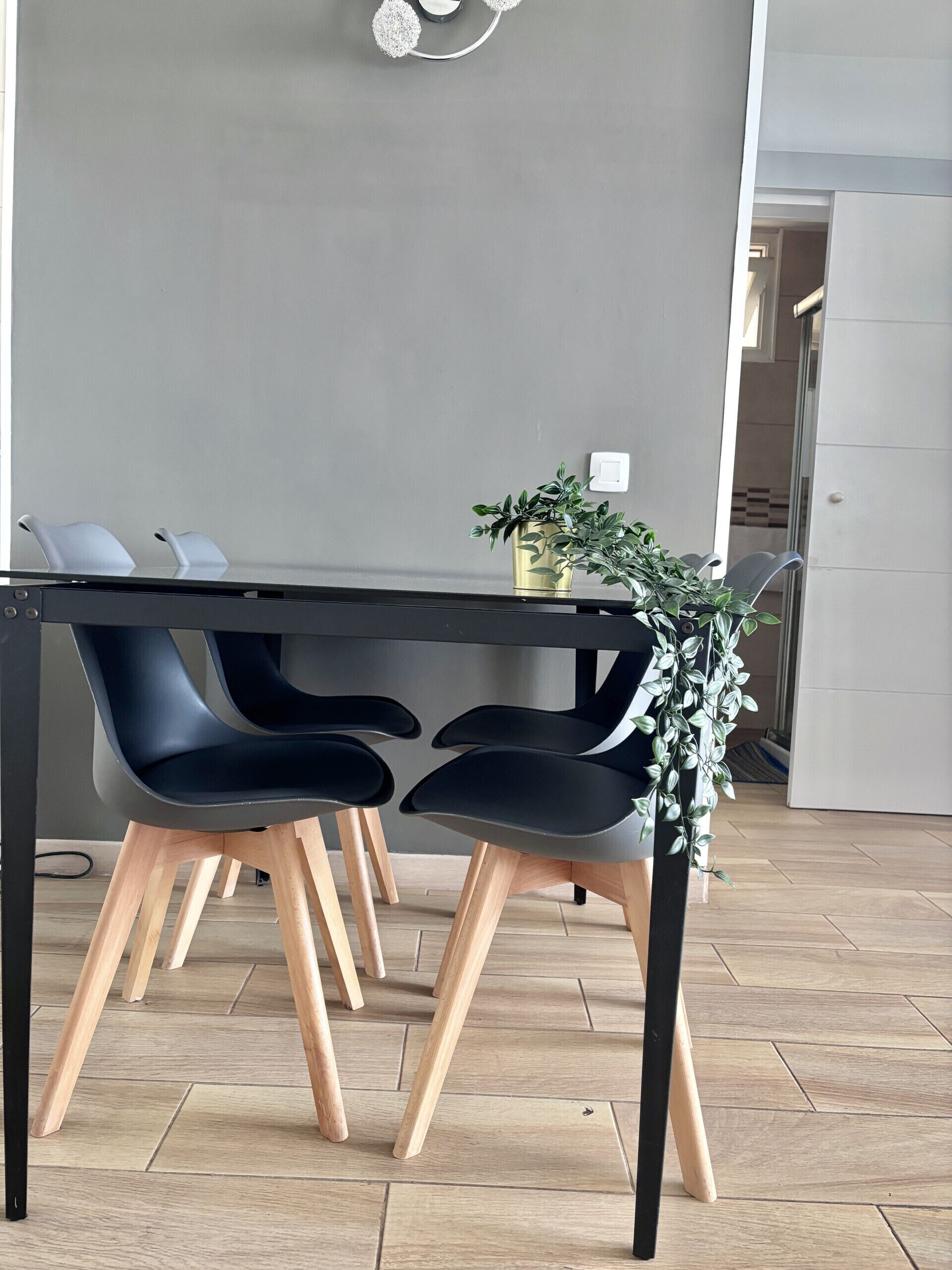 Ein moderner Essbereich mit einem schwarzen Tisch, zwei schwarzen Stühlen mit Holzbeinen und einem Topf mit Grünpflanzen.