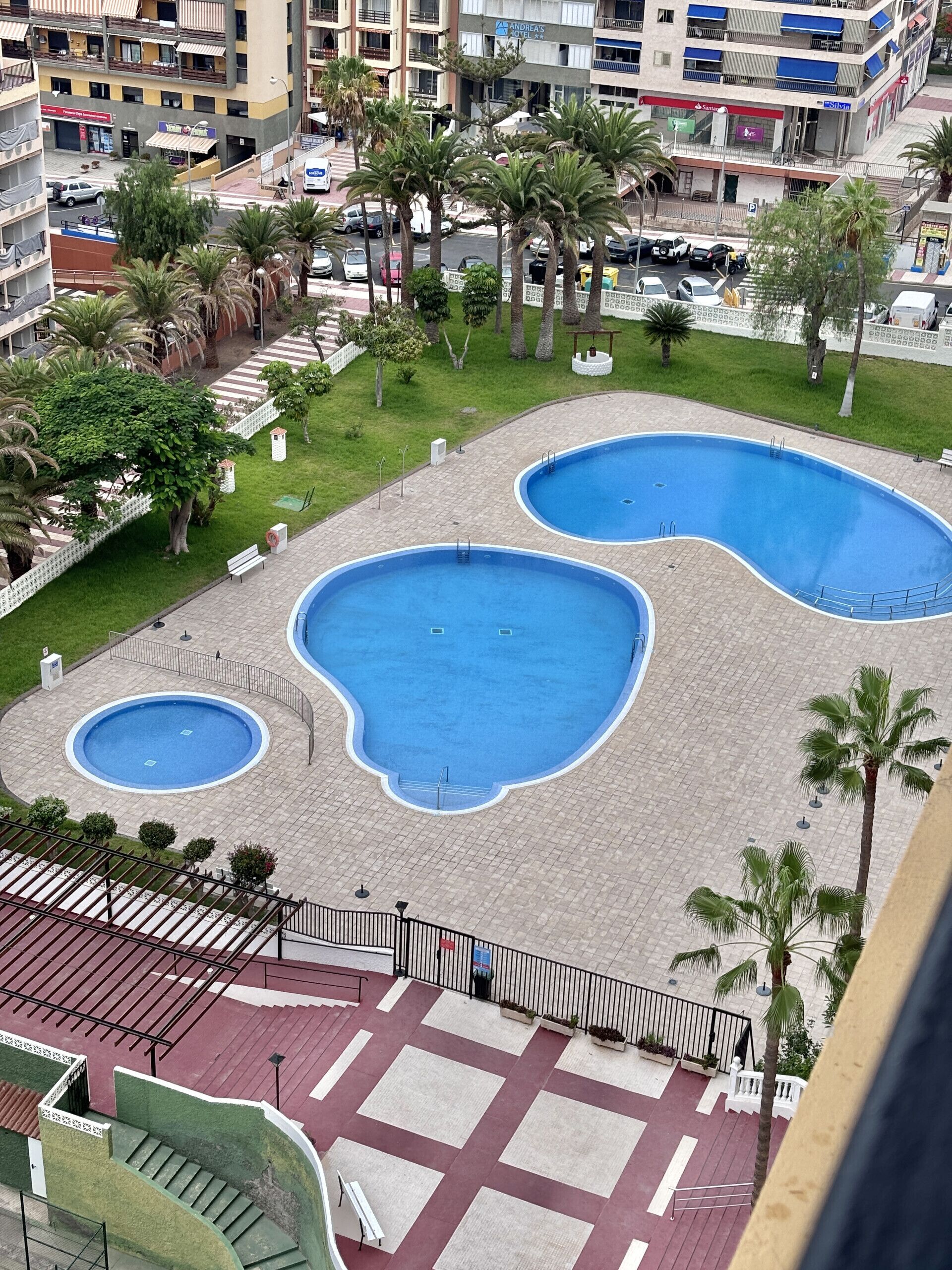 A swimming pool complex with multiple pools, surrounded by palm trees and a paved walkway.