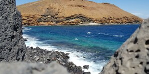 Una costa rocosa con aguas azul cristalino y una montaña al fondo.