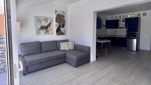 A modern living room with a grey sectional sofa, a dining table with chairs, and a kitchen area with a refrigerator and microwave. - A revisar (Los Cristianos)